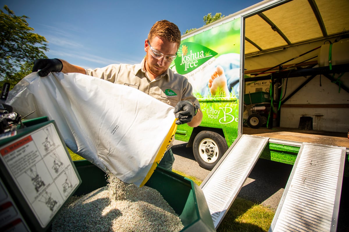 lawn care expert pours fertilizer in spreader